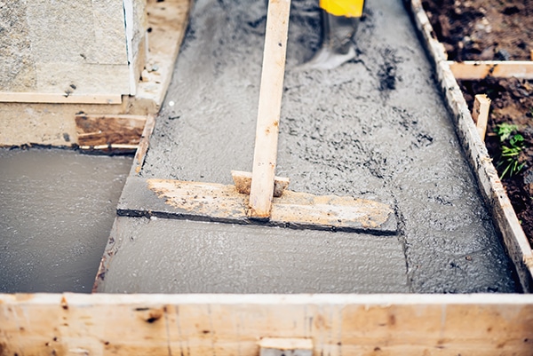 Mason building and leveling a first layer of fresh concrete floor at house stairs and sidewalks, construction site