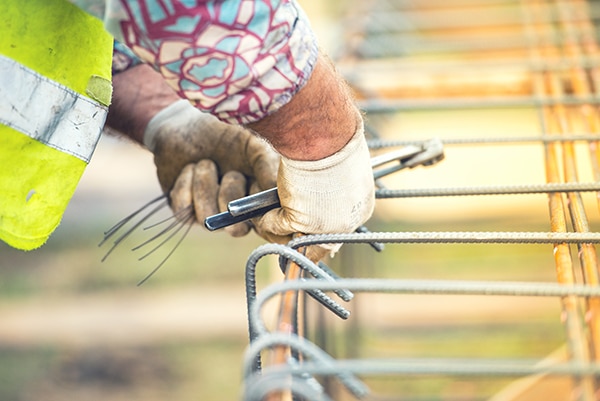 worker hands using steel wire and pincers to secure steel bars, preparing for concrete pouring on construction site