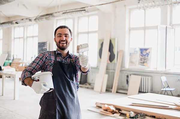 Happy young painter holding paint brush and showing it to camera.